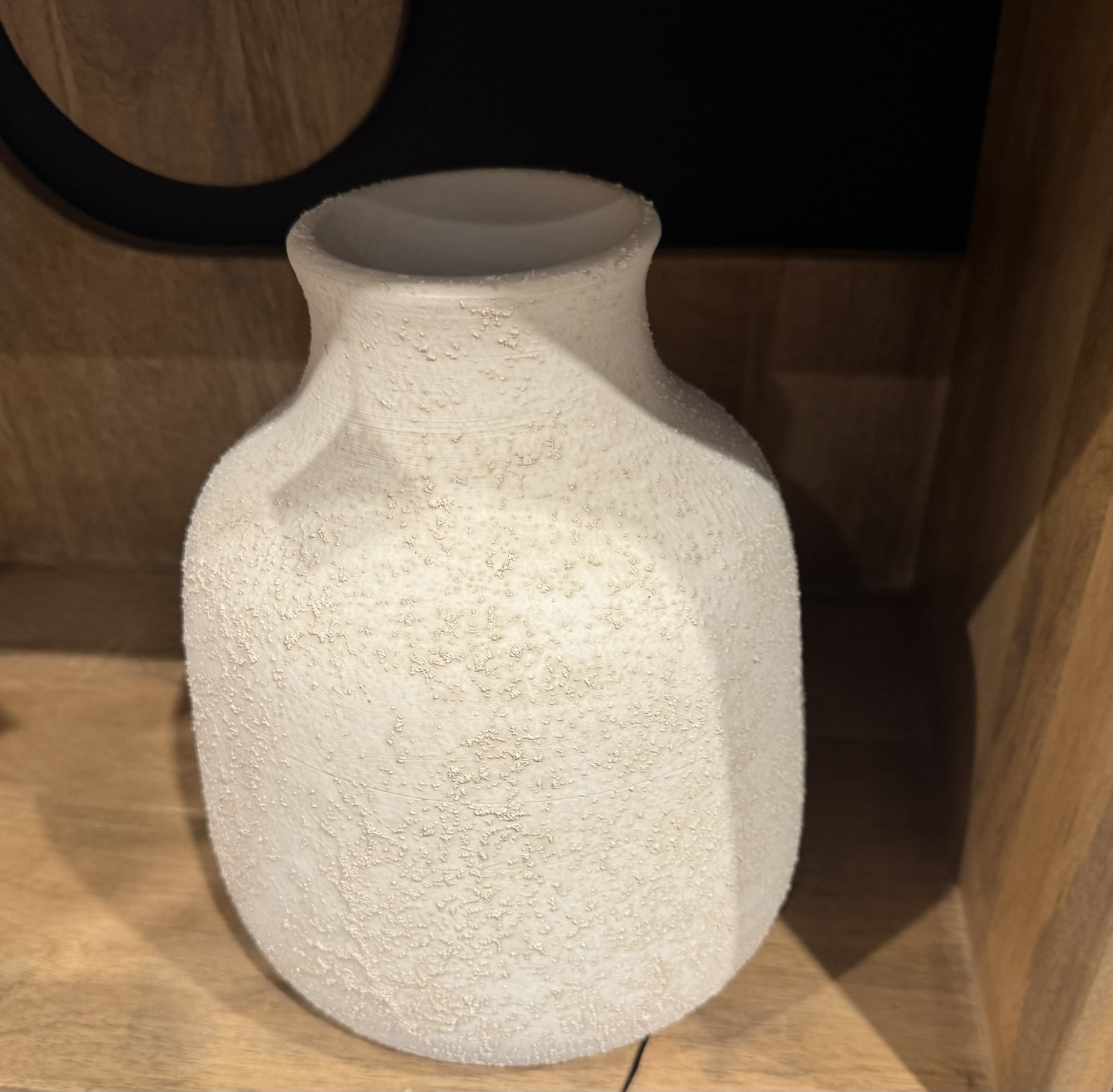 Tom vas i sandtexturerad lera med vinklade axlar i en ljus trähylla